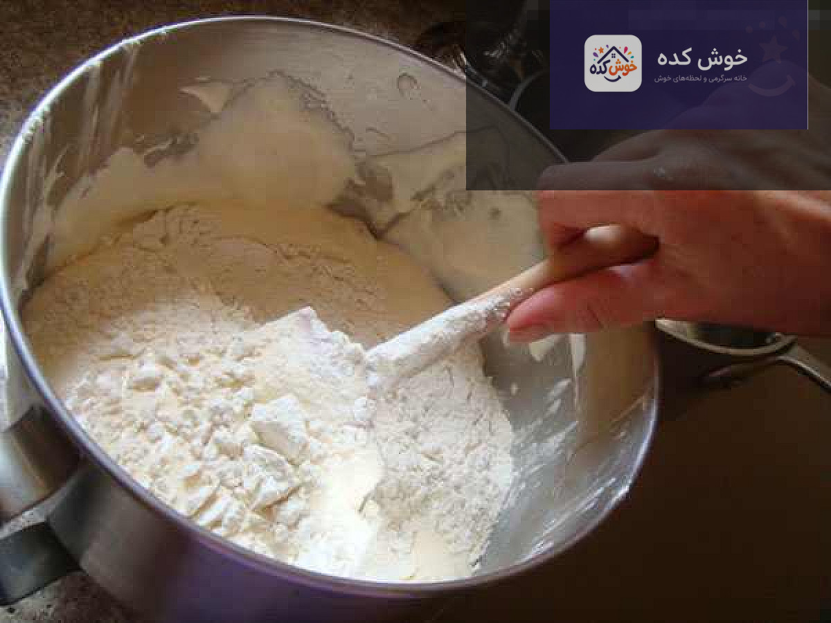 زنی در حال فولد کردن مواد کیک با لیسک در یک کاسه شیشه‌ای