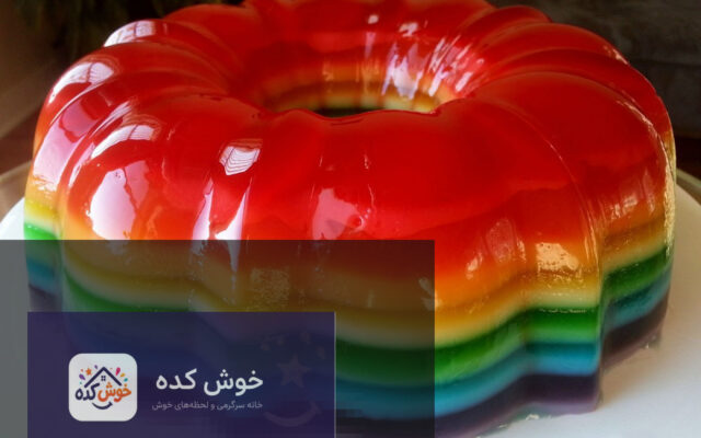 ژله رنگین کمان لایه ای در لیوان، با لایه های رنگارنگ و میوه های تازه تزئین شده، آماده سرو.