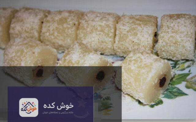مسقطی بیسکویتی با لایه های سفید و قهوه ای، تزیین شده با پودر پسته و گل محمدی، آماده سرو در ظرف شیشه ای