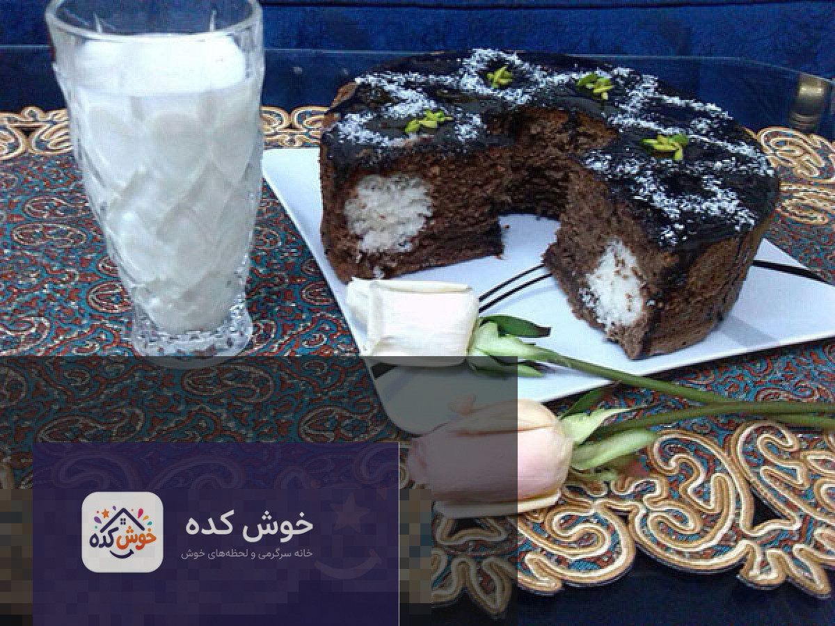 کیک سورپرایز نارگیلی خوش کده کیک سورپرایز نارگیلی برش خورده با لایه های سفید و مغز نارگیل، تزیین شده با پودر نارگیل و گلبرگ های خوراکی